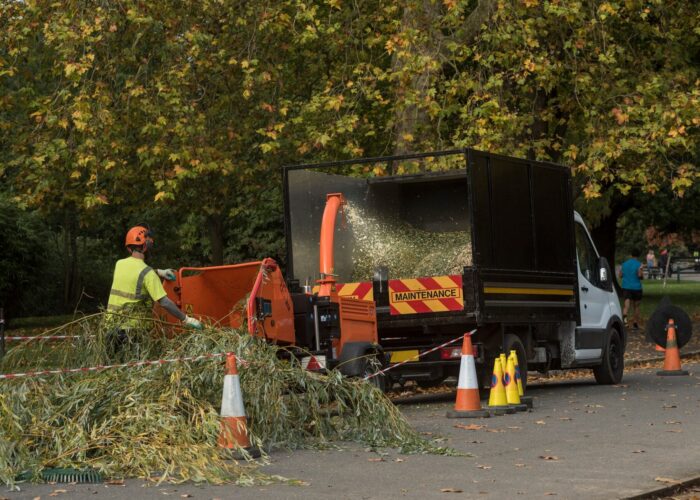A tree surgeon / arborist feeds branches into a heavy duty shredder to become compost / mulch.